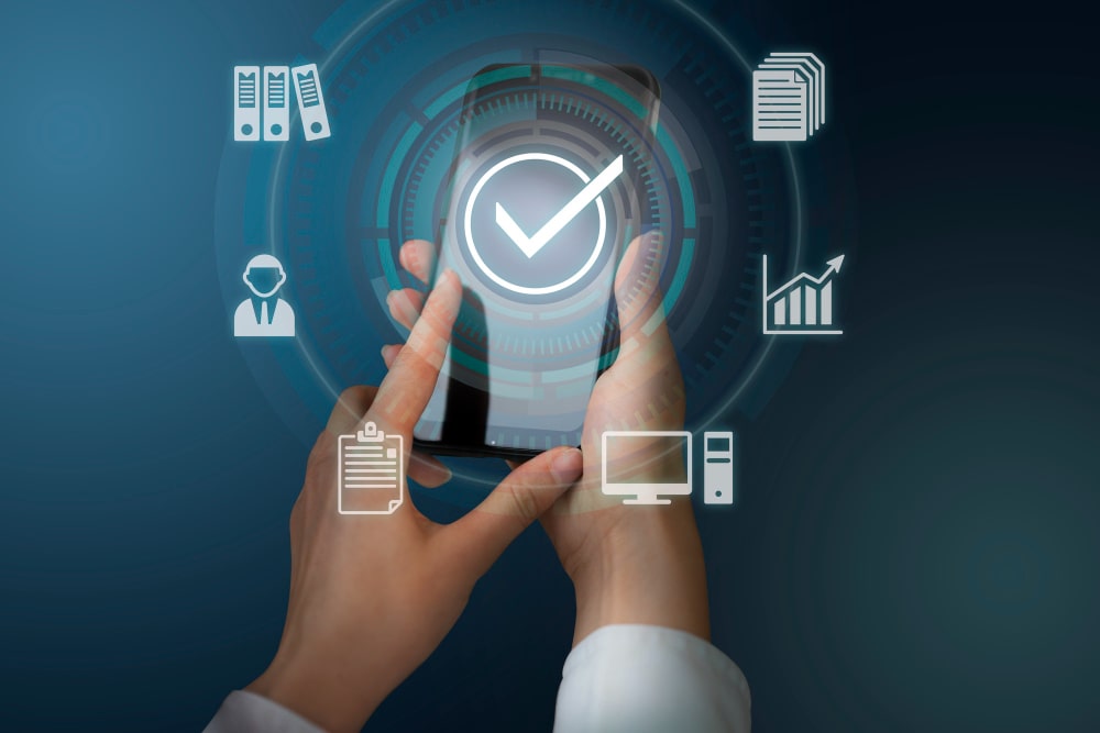 Hände halten ein Smartphone mit digitalem Check-Symbol, umgeben von Icons für Dokumente, Analyse, Computer und Organisation – Symbol für Digitalisierung Prozessen und messbare Effekte